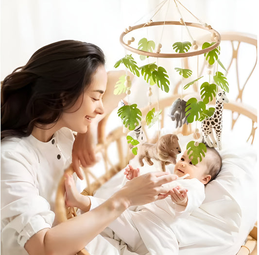 Babymobil med djur och gröna blad ovanför bebis i säng